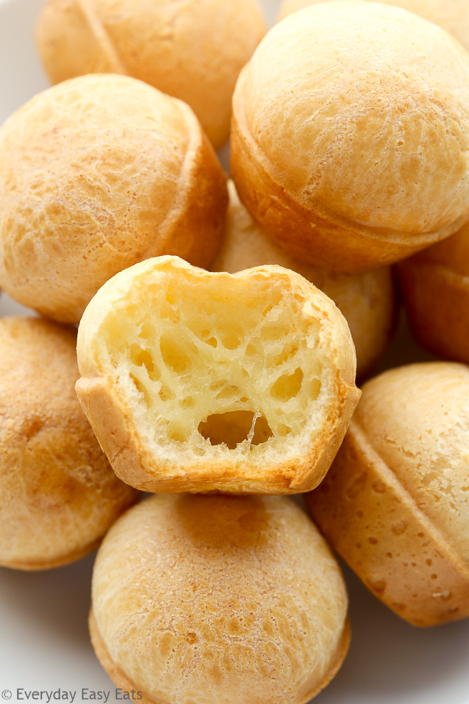 Side view of Brazilian Cheese Bread (Pão de Queijo) in a white plate, one piece has a bite taken out of it.