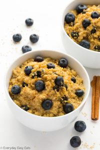 Overhead view of two Healthy Breakfast Quinoa Bowls on a white background with scattered blueberries and cinnamon sticks.