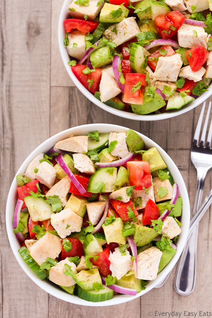 Overhead view of two bowls of Chicken Avocado Salad on a beige background with forks on the side.