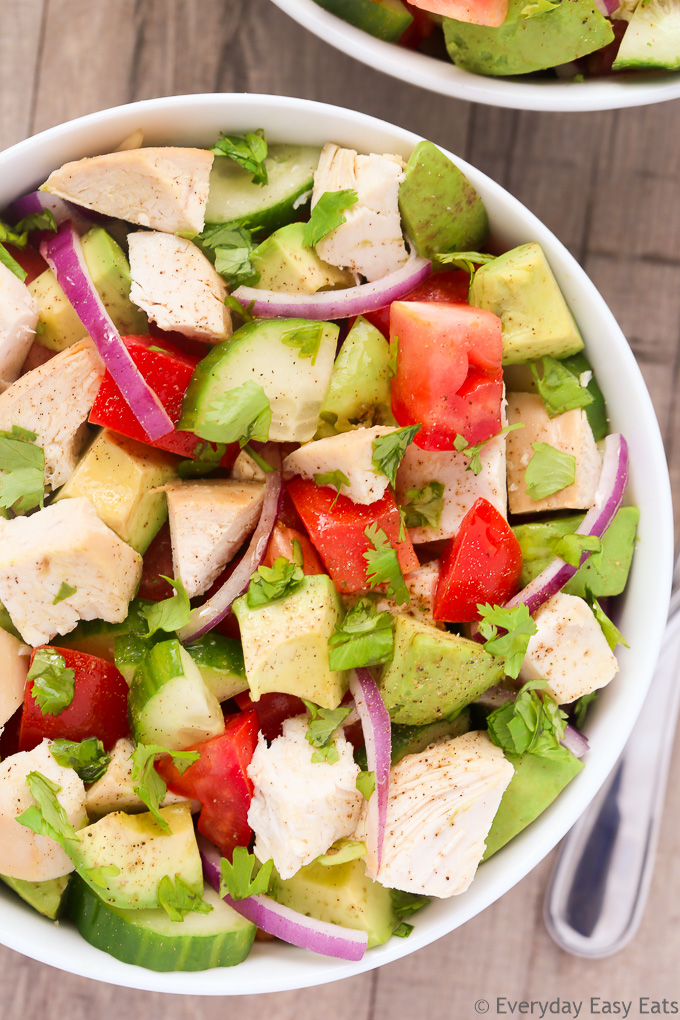 Close-up overhead view of a bowl of Chicken Avocado Salad on a beige background.