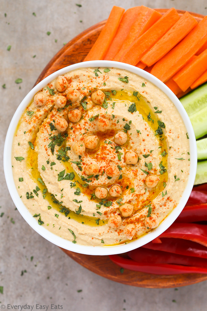 Overhead view of a bowl of Hummus Without Tahini with chopped vegetables on a neutral background.