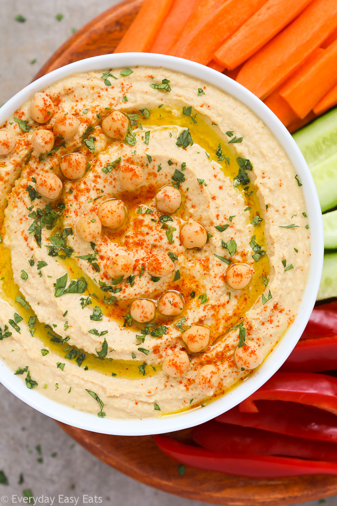 Close-up overhead view of a bowl of Easy Homemade Hummus Without Tahini with chopped vegetables on a neutral background.