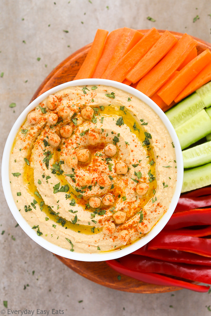 Overhead view of a bowl of Homemade Hummus Without Tahini with chopped vegetables on a neutral background.