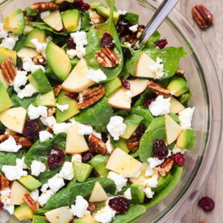 Overhead view of Avocado Spinach Salad in a glass serving bowl on a wooden background.