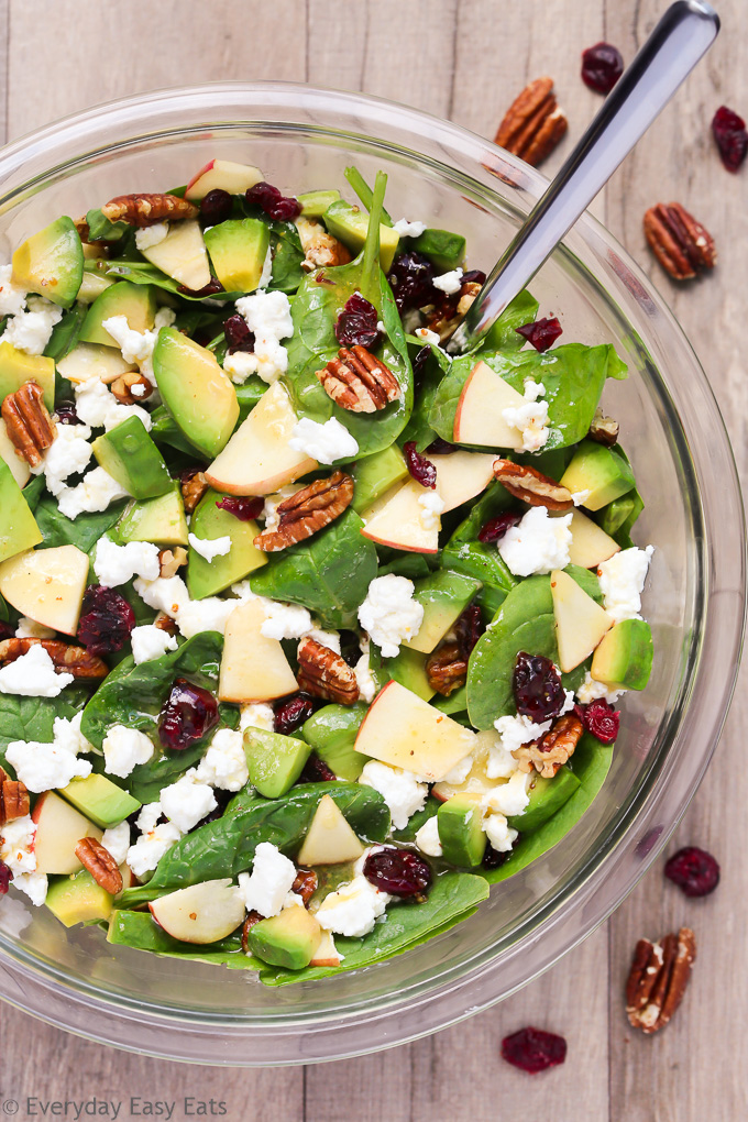 Overhead view of Apple Avocado Spinach Salad in a glass serving bowl on a wooden background.