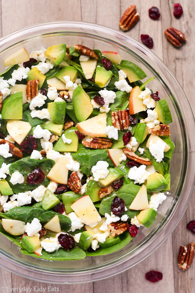 Overhead view of Apple Avocado Spinach Salad in a glass serving bowl on a wooden background.