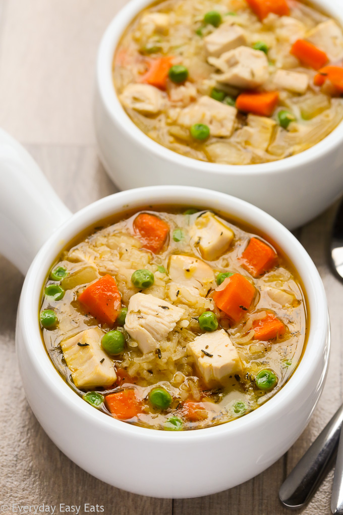 Close-up overhead view of two bowls of One-Pot Chicken and Rice Soup on a beige background.