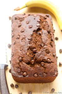 Overhead view of a loaf of Double Chocolate Banana Bread on a wooden chopping board.