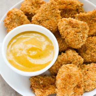 Overhead view of Panko Baked Chicken Nuggets in white plate with a small dipping bowl of honey mustard sauce on the side.
