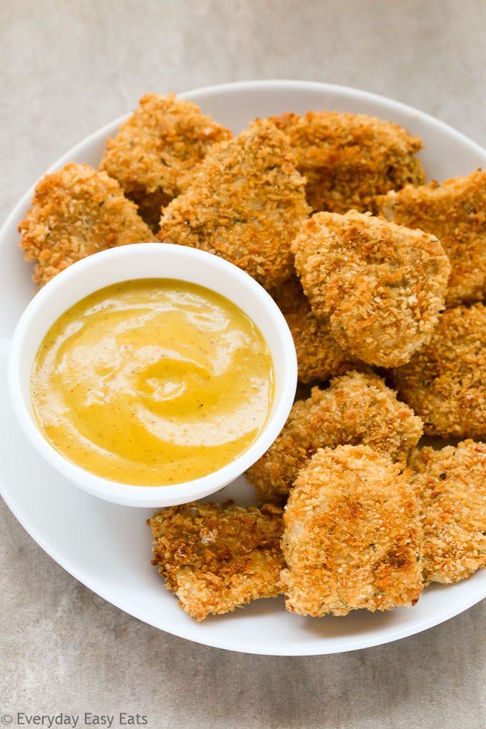 Overhead view of Panko Baked Chicken Nuggets in white plate with a small dipping bowl of honey mustard sauce on the side.