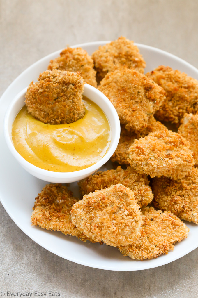 Overhead view of Baked Chicken Nuggets in white plate with a nugget being dipped into the Honey Mustard Sauce on the side.
