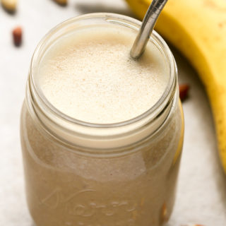 Overhead view of Peanut Butter Banana Protein Shake Recipe in a mason jar with a metal drinking straw against a beige background.