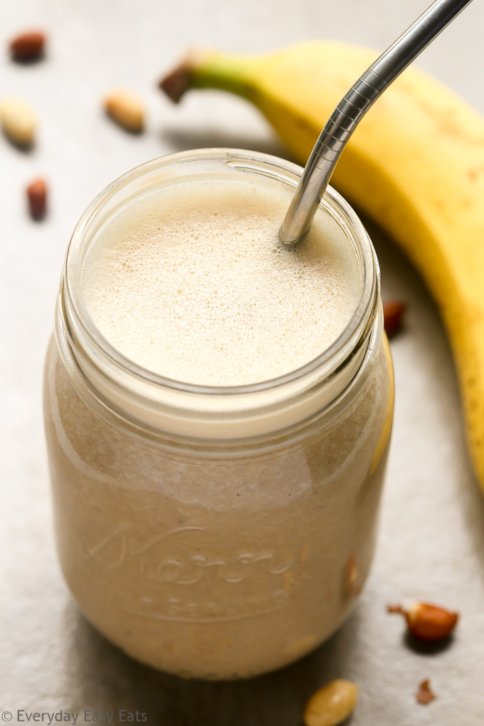 Overhead view of Peanut Butter Banana Protein Shake in a mason jar with a metal drinking straw against a beige background.