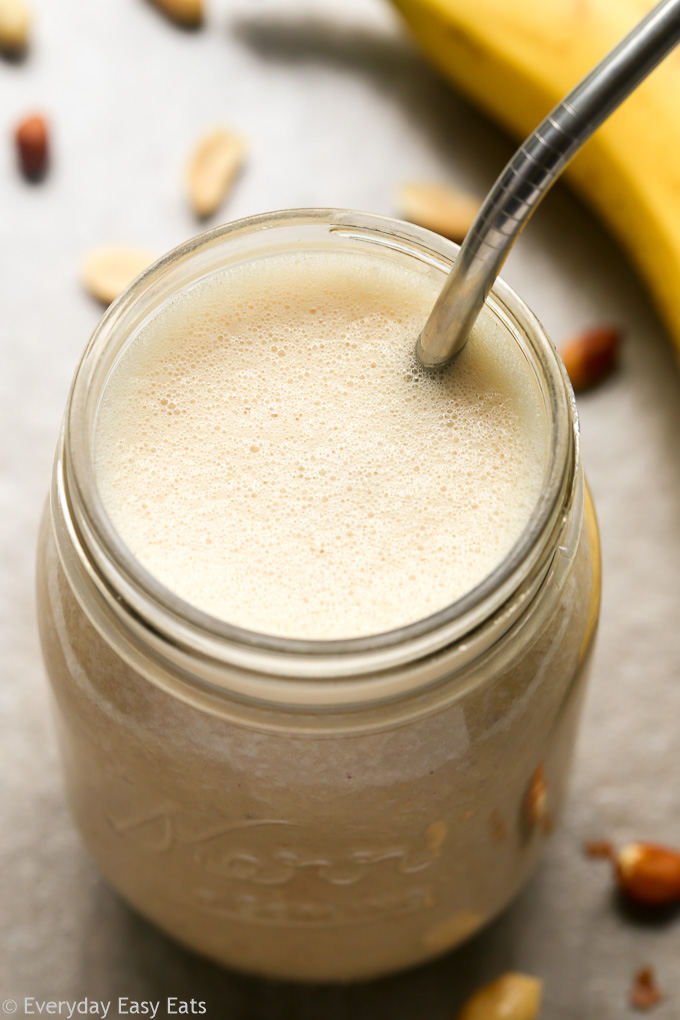Close-up overhead view of Peanut Butter Banana Protein Shake Recipe in a mason jar with a metal drinking straw against a beige background.
