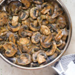 Close-up overhead view of Sautéed Mushrooms and Onions in a skillet with a kitchen towel wrapped around the handle.