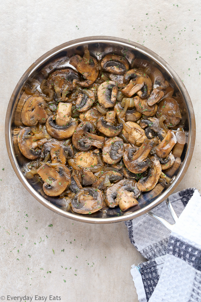 Overhead view of Sautéed Mushrooms and Onions in a skillet with a kitchen towel wrapped around the handle.