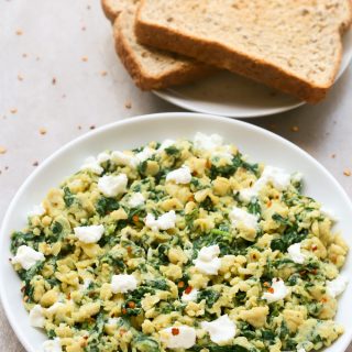 Overhead view of a plate of Scrambled Eggs with Spinach with toast on the side on a neutral-colored surface.