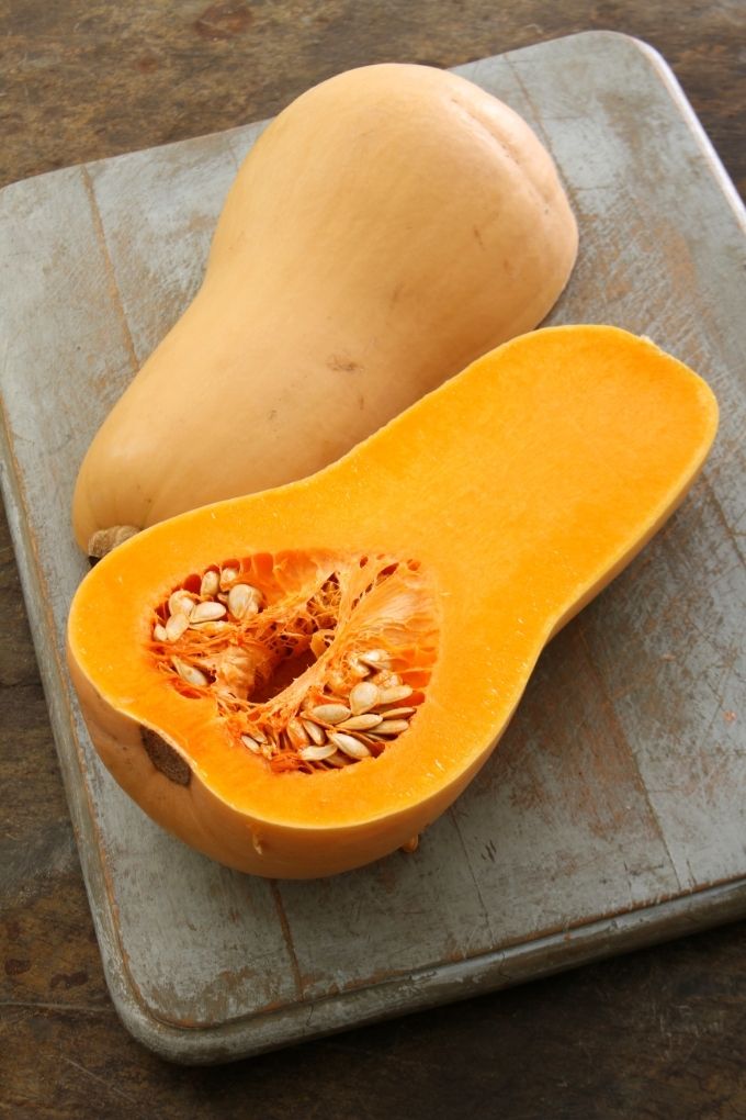 Overhead view of two fresh butternut squash halves on a chopping board.