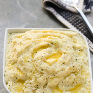 Overhead view of Goat Cheese Mashed Potatoes with a serving spoon on the side on a grey background.