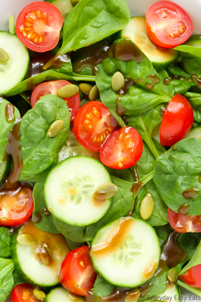 Overhead view of Tomato Spinach Salad in a white bowl against a light background.