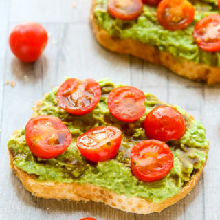 Side overhead view of two slices of Tomato Avocado Toast with scattered cherry tomatoes on a wooden background.