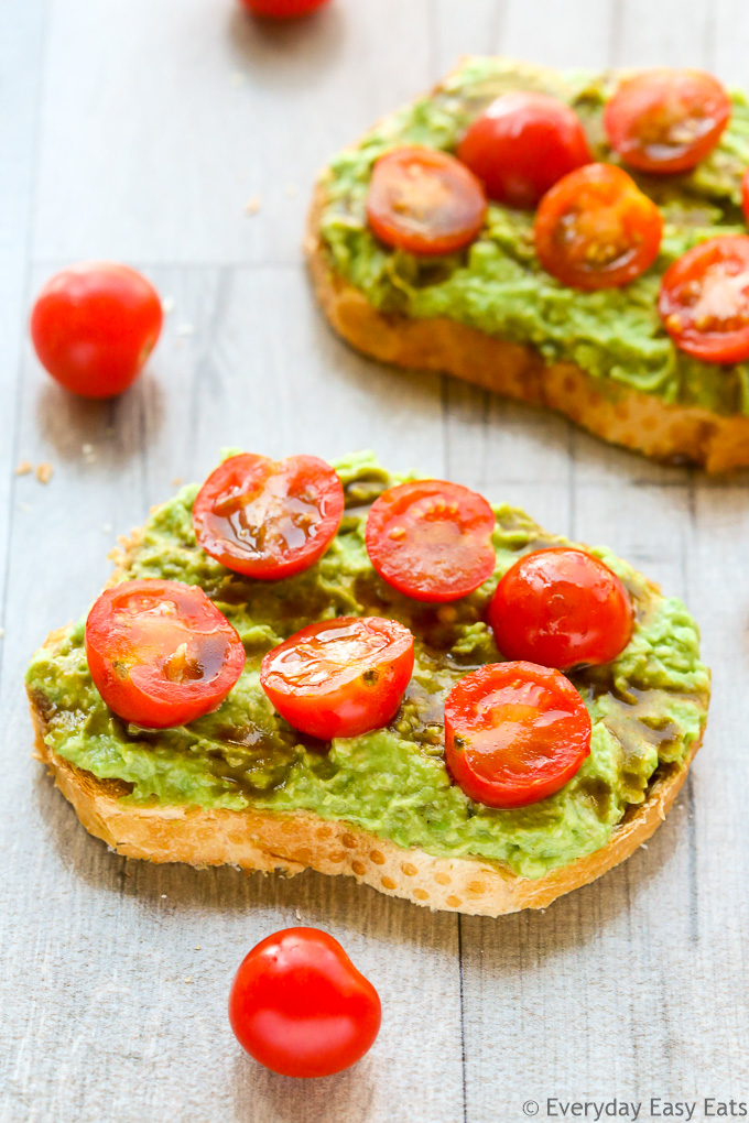 Side overhead view of two slices of Tomato Avocado Toast with scattered cherry tomatoes on a wooden background.