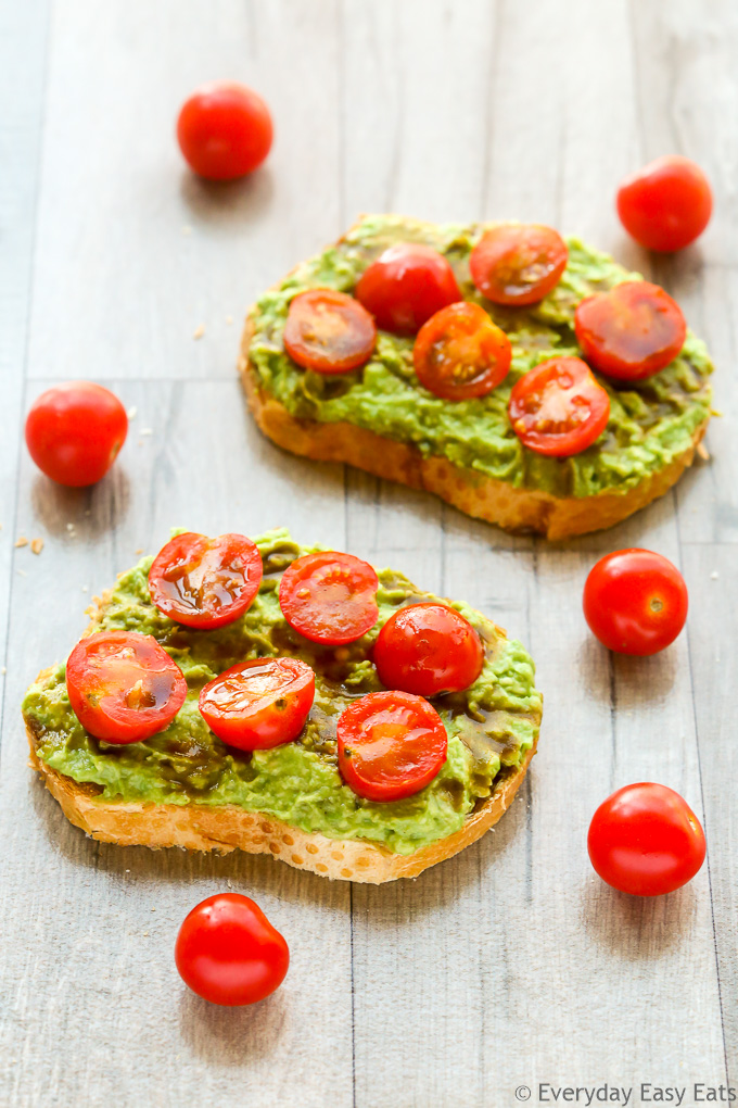 Overhead view of two slices of Tomato Avocado Toast with scattered cherry tomatoes on a wooden background.