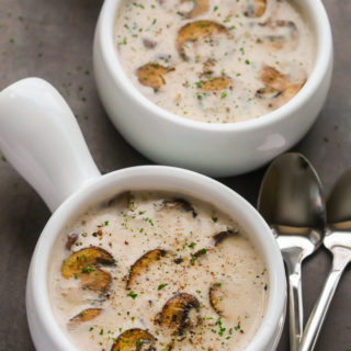 Overhead view of two bowls of Cream of Mushroom Soup on a dark background with two spoons on the side.