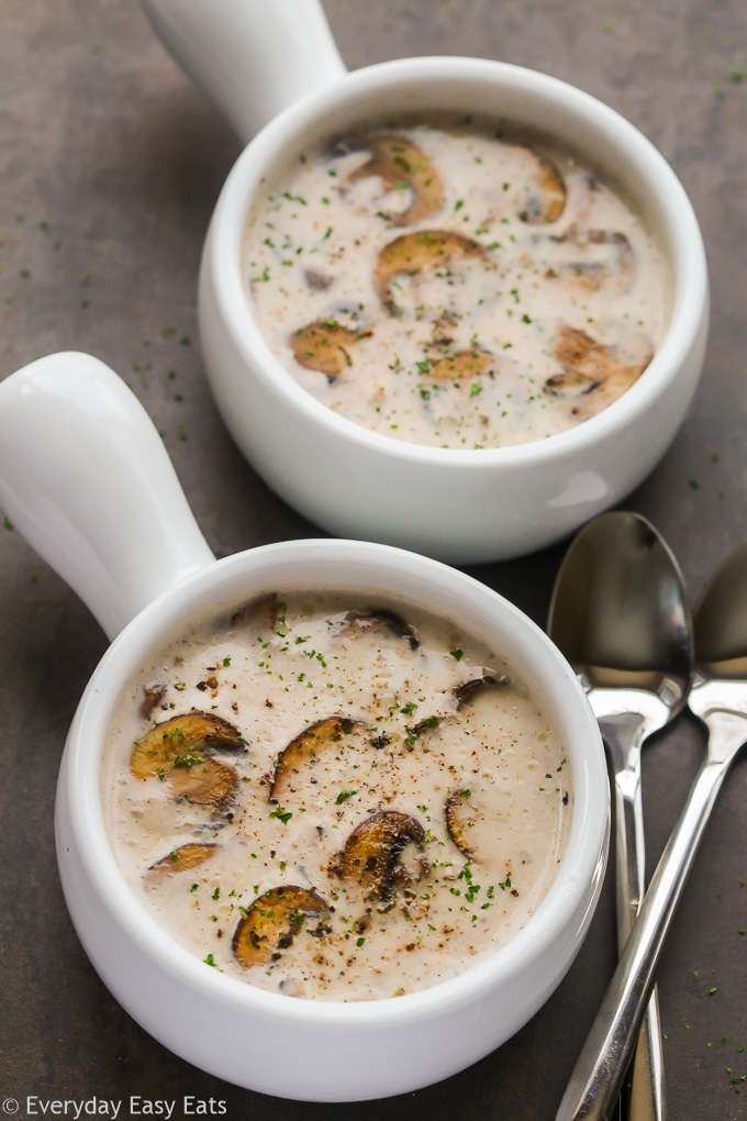 Overhead view of two bowls of Creamy Mushroom Soup on a dark background with two spoons on the side.
