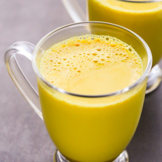 Close-up overhead view of two glass mugs filled with Golden Latte (Turmeric Milk) on a dark surface.