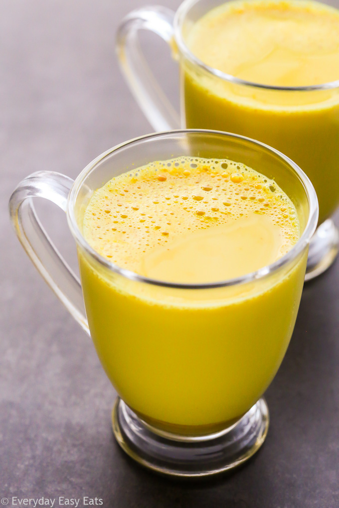 Close-up overhead view of two glass mugs filled with Golden Latte (Turmeric Milk) on a dark surface.