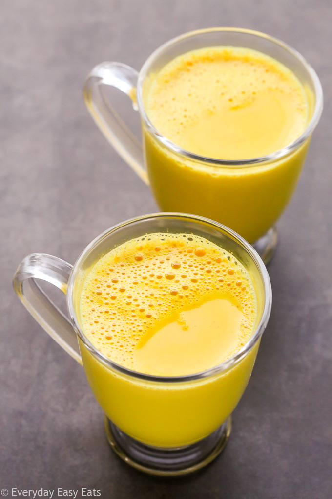 Overhead view of two glass mugs filled with Golden Latte (Turmeric Milk) on a dark surface.