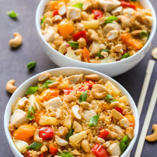 Overhead view of two bowls of Pineapple Chicken Coconut Rice on a dark background with chopsticks on the side.