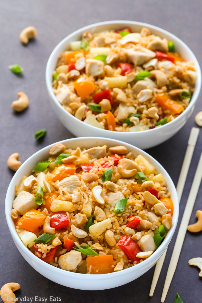 Overhead view of two bowls of Pineapple Chicken Coconut Rice on a dark background with chopsticks on the side.