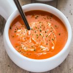 Overhead view of Creamy Tomato Soup in a white bowl on a wooden background with title text overlay.
