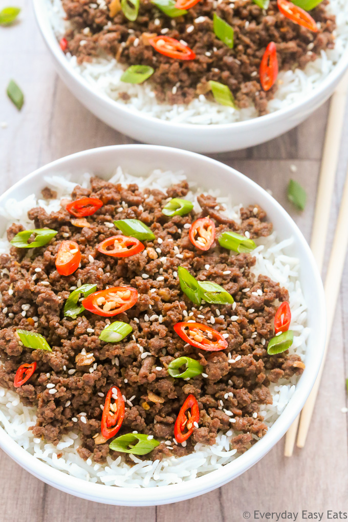 Close-up overhead view of two bowls of Bulgogi Ground Beef with rice on a wooden surface with chopsticks on the side.