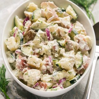 Overhead view of Creamy Dill Potato Salad in a large white serving bowl on a grey surface.