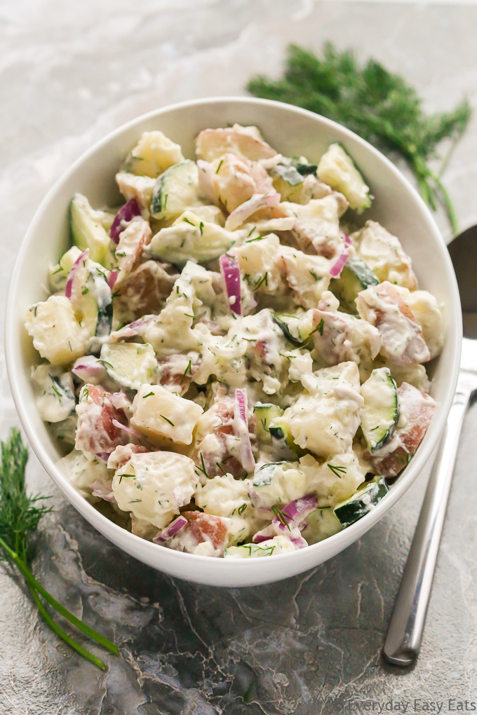 Overhead view of Creamy Dill Potato Salad in a large white serving bowl on a grey surface.