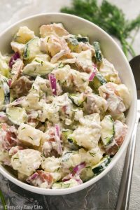 Close-up overhead view of Creamy Dill Potato Salad in a large white serving bowl on a grey surface.