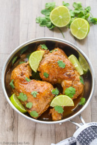 Overhead view of Honey Lime Chicken in a silver skillet with sliced limes on the side.