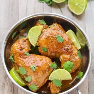 Overhead view of Honey Lime Chicken in a silver skillet with sliced limes on the side.