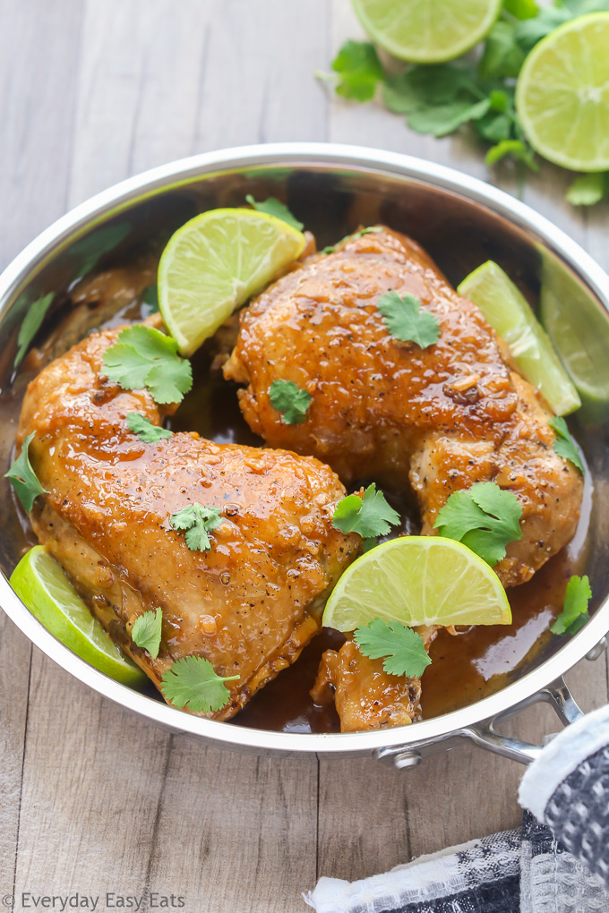 Close-up side overhead view of Honey Lime Chicken in a silver skillet with sliced limes on the side.