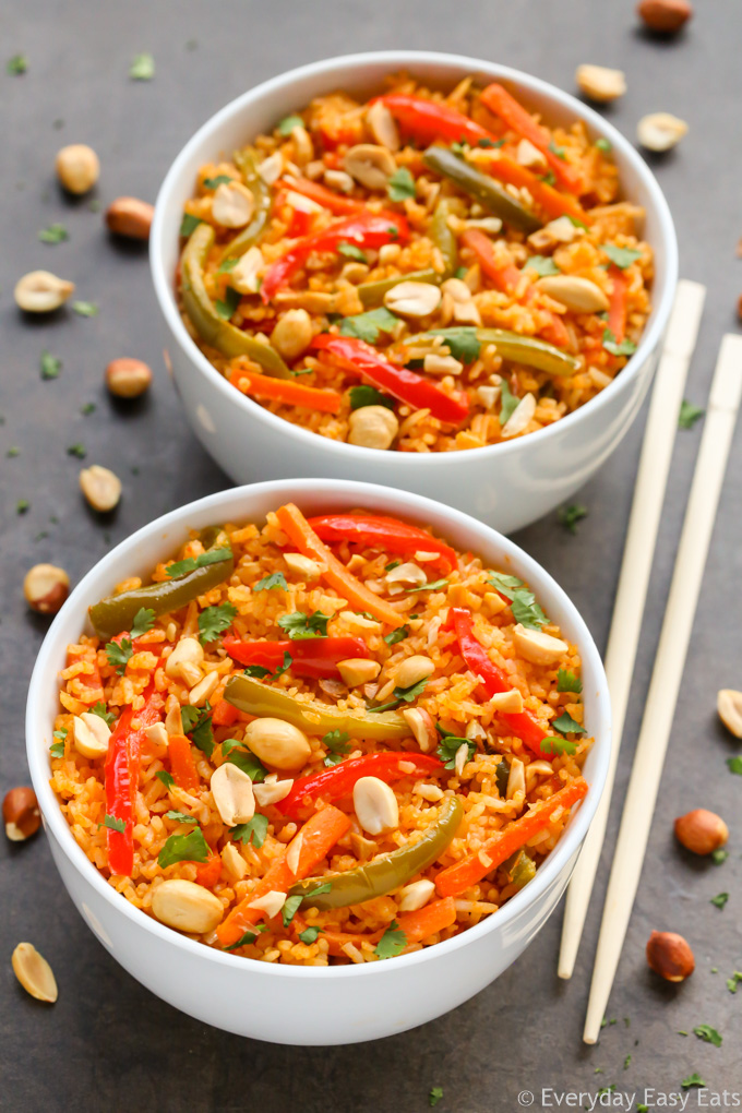 Easy Asian Rice Recipes for Dinner: Two bowls of Thai Coconut Curry Rice with chopsticks, scattered peanuts, and cilantro on a dark background.