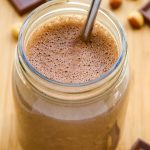 Overhead view of a glass of Chocolate Peanut Butter Protein Shake with straw on a wooden surface.