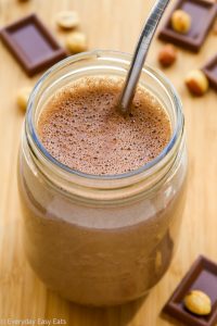 Overhead view of a glass of Chocolate Peanut Butter Protein Shake with straw on a wooden surface.