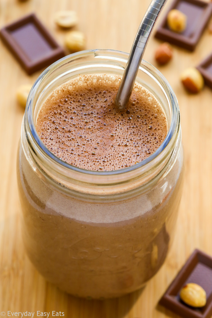 Overhead view of a glass of Chocolate Peanut Butter Protein Shake with straw on a wooden background.