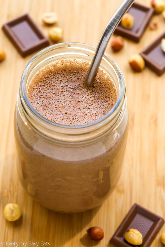 Close-up overhead view of a glass of Chocolate Peanut Butter Protein Shake with straw on a wooden surface.
