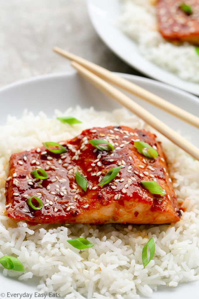 A plate of Baked Honey Sriracha Salmon sitting on a bed of white rice with chopsticks.