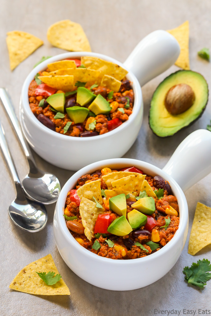 Overhead view of two bowls of Ground Turkey Chili with spoons on the side on a beige background.