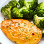 Close-up overhead view of Baked Honey Mustard Chicken Breasts in a white plate with steamed broccoli.